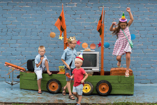 Happy Brothers-boys in colored clothes and girl celebrate birthday of youngest boy on pirate ship. Girl and boy are dressed in carnival hat for parties. Children are happy together. 3 years old