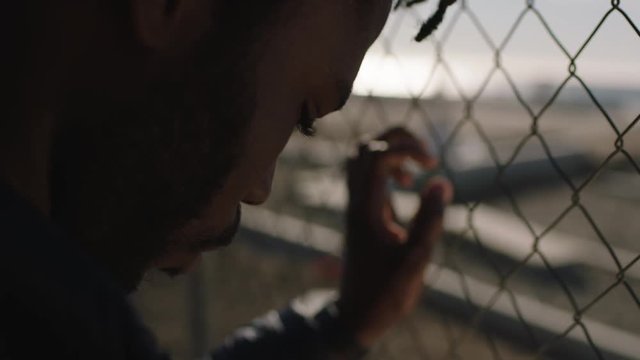 close up portrait of young african american man hands holding fence looking at ocean seaside pensive thinking contemplative