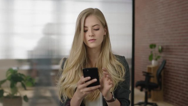 portrait of attractive young blonde woman executive texting browsing using smartphone mobile networking app in modern office workspace
