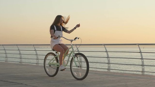 Young attractive woman riding vintage bike near the sea during sunrise or sunset