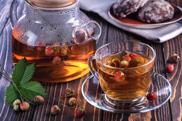 In a mug and teapot berry tea from a forest strawberry, plate with dessert on a wooden table top.Healthy drink from strawberries.