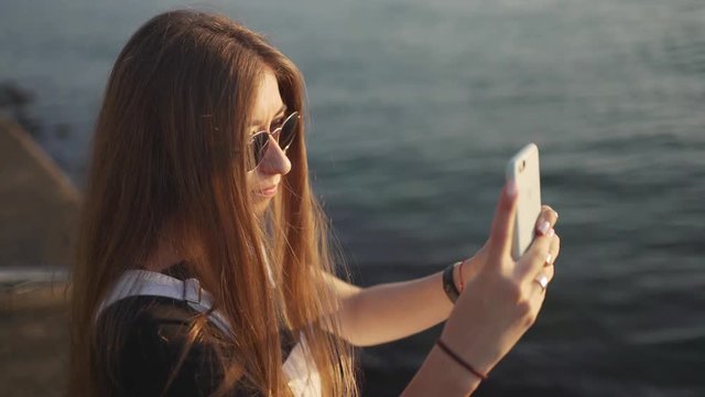 young attractive woman taking pictures of sea at sunset or sunrise 