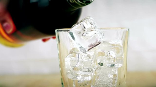 barman pouring whiskey in the glass with ice cubes on wood table background, focus on ice cubes, whisky relax time, gold warm atmosphere