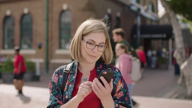 portrait of young blonde woman texting browsing using smartphone social media app wearing glasses in urban background
