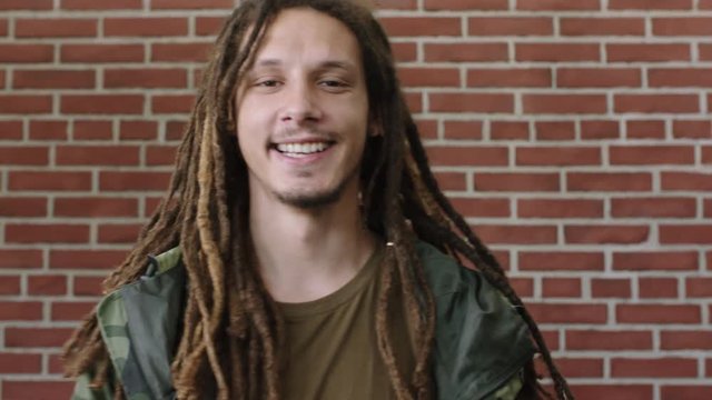 portrait of attractive young mixed race man with dreadlocks laughing cheerful relaxed looking at camera