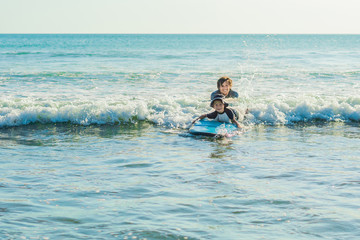 Father teaching his young son how to surf in the sea on vacation or holiday. Travel and sports with children concept