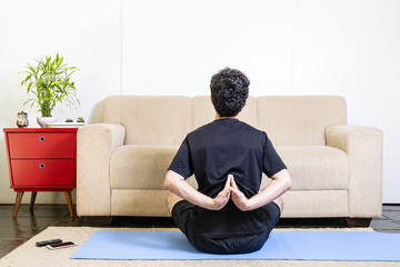 Beautiful caucasian bearded man in black clothes on blue yogamat doing namaste mudra  backwards