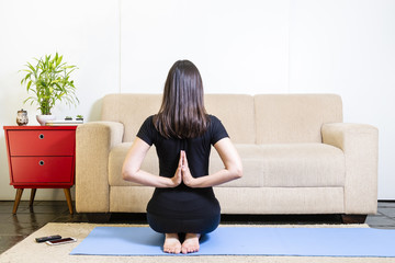 Beautiful caucasian brunette woman in black clothes on blue yogamat doing namaste mudra backwards