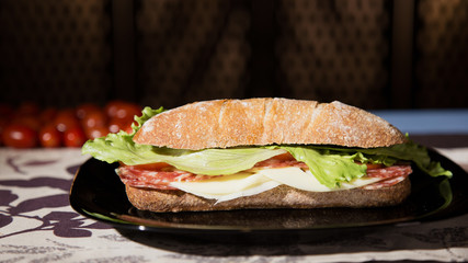 Ciabatta bread sandwich in a decorated table with cherry tomatoes in the background. 