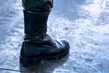 Army / Navy military boot with jungle camouflage pants in top boot standing on dirty polished cement floor