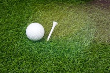 Golf ball and tee are on green grass