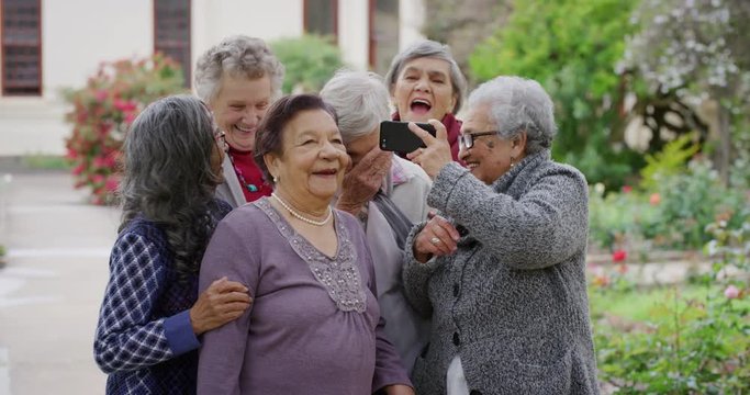 group of diverse elderly women using smartphone taking selfie photo laughing cheerful enjoying carefree retirement lifestyle in beautiful garden outdoors