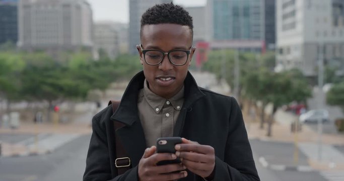 portrait young african american man student using smartphone in city texting browsing messages on mobile phone looking around enjoying urban lifestyle slow motion