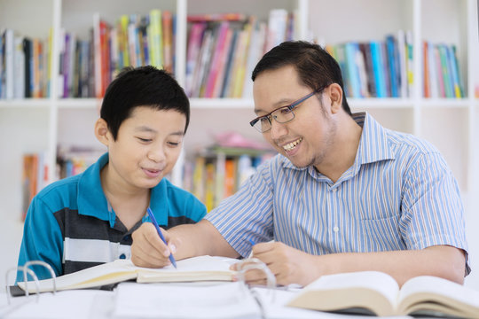 Asian teacher helping his student to read a book
