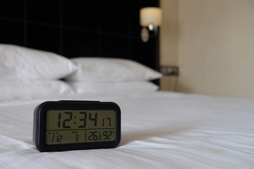 Large digital black clock on white bed in luxury bedroom