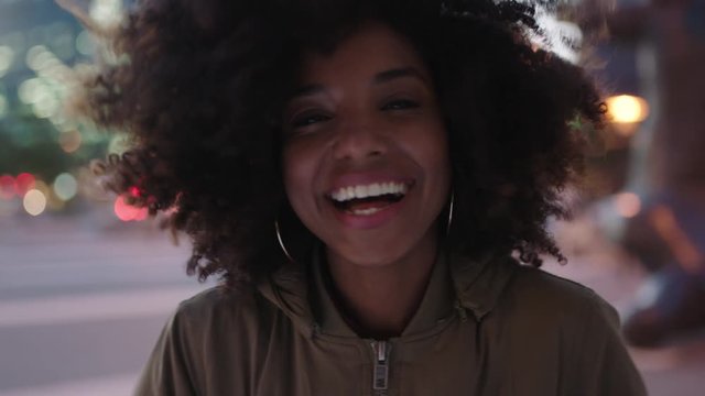 portrait of stylish young black woman with afro laughing playful enjoying night life in city wind blowing hair urban lifestyle