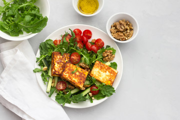 Fresh salad from arugula, cherry tomatoes, cucumbers and roasted cheese on a gray stone background. top view. delicious healthy food. free space