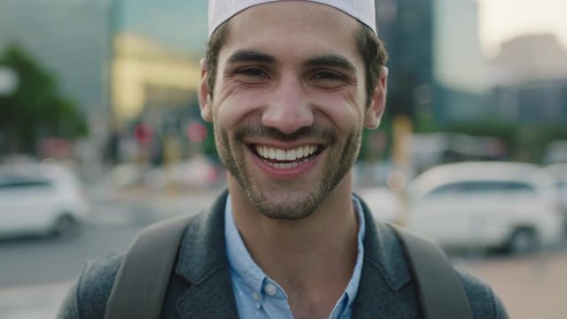 close up portrait of successful young middle eastern businessman smiling looking at camera happy enjoying  urban lifestyle in busy city wearing kufi hat