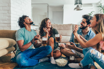 Friends eating popcorn and drinking beer mug at home, having fun.