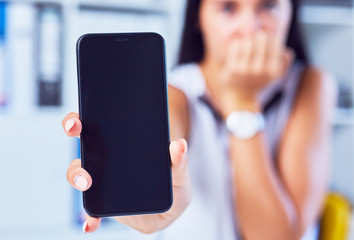 Young sad woman showing a blank smartphone screen. Focus on smartphone. Free space for your message.