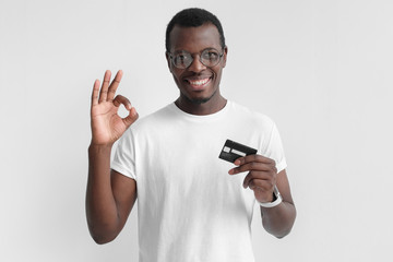 Portrait of young smiling dark skin african american man in white t shirt holding credit card and...