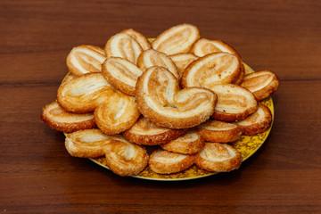 Palmier biscuits - french cookies made of puff pastry (also called palm leaves, elephant ears or french hearts) in a plate on wooden table
