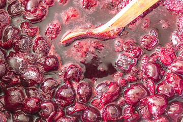 Cooking cherry jam.Constantly stir with a wooden spoon swirling dark red cherries and white sugar....