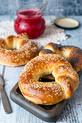 Homemade baking. Fresh ruddy round bagels with sesame and a jar of fruit jam on an old wooden table.