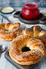 Homemade baking. Fresh ruddy round bagels with sesame and a jar of fruit jam on an old wooden table.