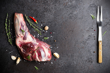 Raw fresh Lamb Meat shank, herbs and fork on black stone background