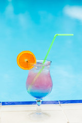 Glass with cocktail on the edge of resort swimming pool. Vacations concept.