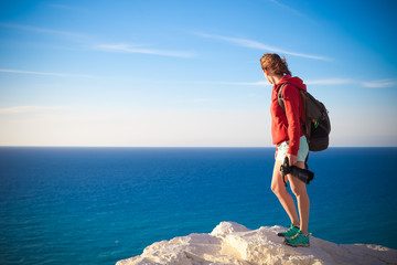 Young professional photographer woman stands with photo camera in hands on rock above the sea, beautiful nature, profession, vacation and travel concept
