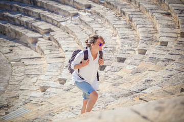 Young woman tourist with a backpack on the background of the steps of an ancient Greek amphitheater, vacation and travel