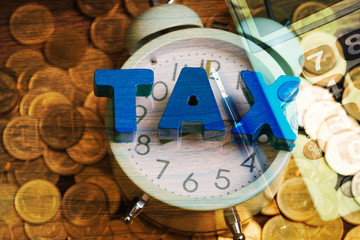 Time to pay TAX concept. TAX alphabet with stack of coin and vintage alarm clock with office supplies or office work essential tools or items