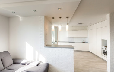 White lamps above kitchen island under a window with bar stools in bright room