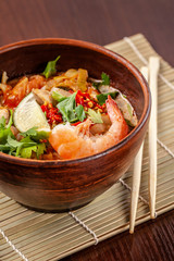 Asian Oriental Cuisine. Japanese spicy soup with seafood, shrimps, vegetables, lime, parsley, and hot pepper, in a plate of red clay, stands on a table in a restaurant. Copy space, selective focus