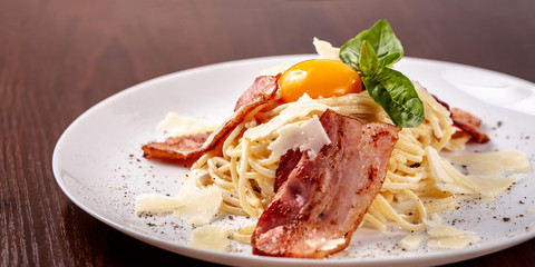 Italian pasta spaghetti carbonara, with fried bacon, parmesan cheese and egg yolk. It is on the table in the restaurant. Copy space, selective focus