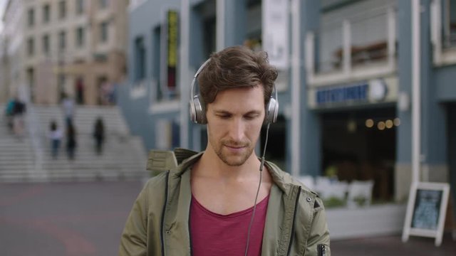 portrait of young attractive caucasian man in busy urban street using smartphone texting wearing headphones listening to music enjoying lifestyle