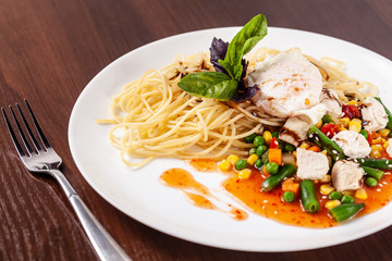 Italian pasta Spaghetti with vegetables and chicken. With red salsa sauce and basil. It is on the table in the restaurant. Copy space, selective focus