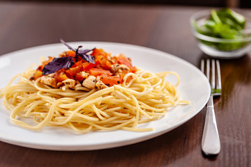 Italian pasta spaghetti with red tomato sauce, tomatoes and grilled chicken. It is on the table in the restaurant. Copy space, selective focus