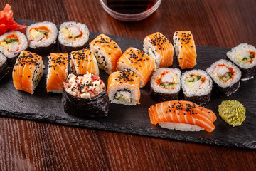 Asian traditional cuisine. A large set of rolls and sushi on a black slate stone, on a wooden table in a restaurant, with soy sauce and Chinese chopsticks.