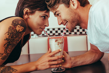Romantic couple sharing milk shake using straws from the same gl - obrazy, fototapety, plakaty