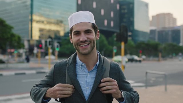 portrait of successful young middle eastern man smiling looking at camera happy enjoying  urban lifestyle in city wearing kufi hat