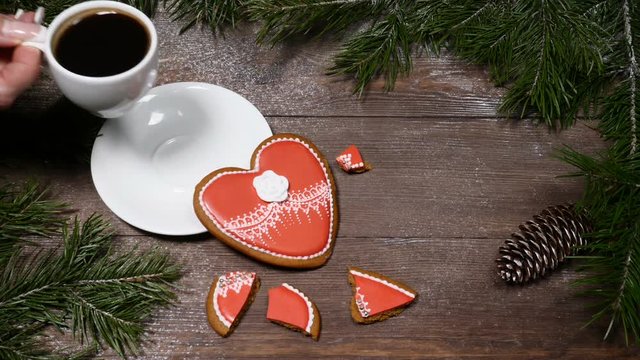 Food art. Broken heart. Fir tree, a cup of fresh-brewed coffee and heart-shaped gingersnaps placed on wooden background.one cookie is broken into pieces Top view. Female hands takes out a cup
