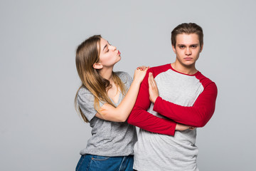 Portrait of young displeased man gesturing to stop with hand while beautiful woman kissing his cheek isolated over white background