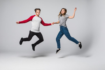 Fototapeta na wymiar Full length portrait of a cheerful young couple jumping and running over white wall