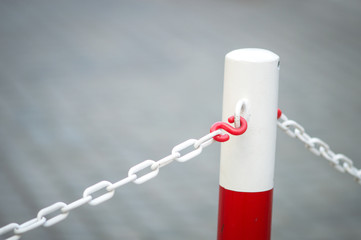 Metal barrier pole painyed in bright red and white with white chain attached at both sides. Copy space on grey background