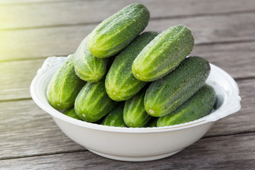 whole green cucumbers in a large white antique plate on a wooden table