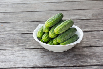 whole green cucumbers in a large white antique plate on a wooden table