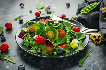 Summer salad with edible flowers, spinach, blueberries, raspberry, sweet peas, cherry tomatos and...
